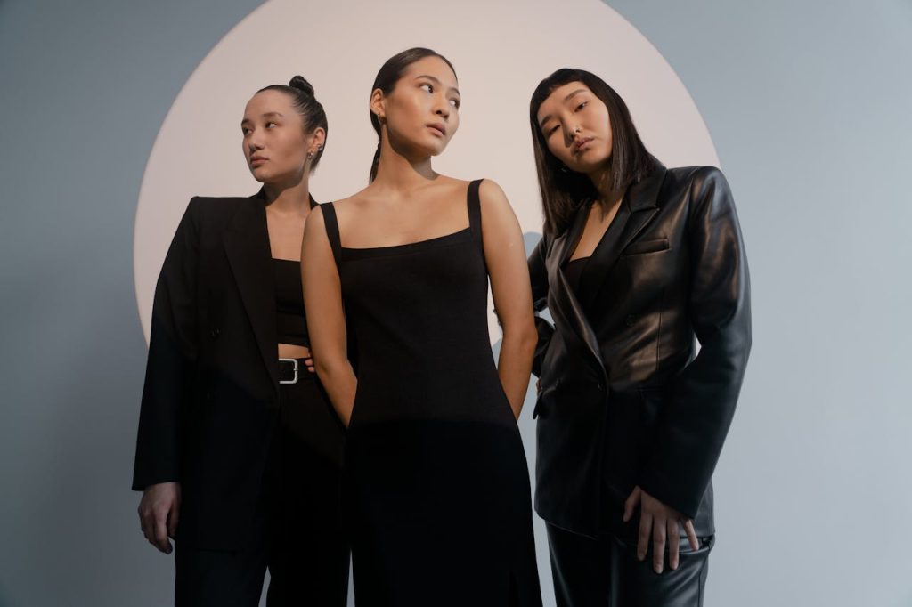 women-wearing-black-clothes-7871156 Three women in sleek outfits pose confidently under artistic lighting for a modern portrait.